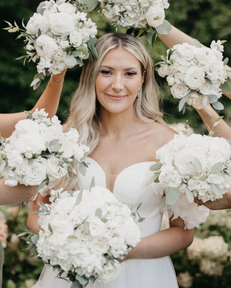 A bride posing for a picture while her bridesmaids hold up their bouquets to frame her face